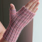 A hand wearing Lisa's Knits' Fingerless Gloves and Mitts, Fingering Weight, in pink is shown against a neutral background. The mitt features a ribbed texture and covers only the thumb, leaving the fingers free.