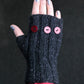 A hand wearing a black Lisa's Knits Fingerless Glove, adorned with three red buttons on the back. The hand's nails are painted with silver polish, and the background is dark. This winter accessory covers the wrist and part of the forearm, providing stylish warmth.