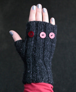 A hand wearing a black Lisa's Knits Fingerless Glove, adorned with three red buttons on the back. The hand's nails are painted with silver polish, and the background is dark. This winter accessory covers the wrist and part of the forearm, providing stylish warmth.