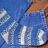 A pair of Lisa's Knits Basic Toe-Up Socks, featuring alternating vertical stripes of white and dark blue, are partially folded on top of each other and lying on a wooden surface.