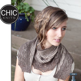 A person with wavy, short hair sits on a porch, draped in the Alby Shawl—a crescent-shaped piece featuring an elegant lace pattern in shades of grey and brown. The person is looking to the side. In the top left corner, there is a "Chic Knits" logo, and a PDF icon appears at the bottom right.