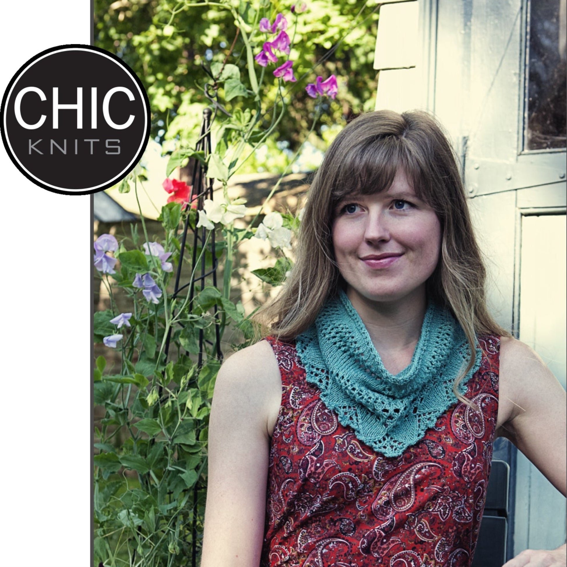 A woman with long hair stands in a garden next to a wooden structure, wearing a red patterned sleeveless top and the turquoise Boelle Cowl from Chic Knits. The cotton blend top exudes comfort and style. The top left corner shows the text "CHIC KNITS" in a black circle. Flowers bloom beautifully in the background.