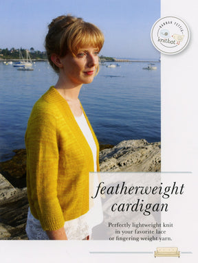 A woman stands outdoors by a calm lake, wearing a light yellow Knitbot Featherweight Cardigan from Never Not Knitting over a white dress. The text on the image reads "Perfectly lightweight knit in your favorite lace or fingering weight yarn." The lake reflects a clear blue sky.