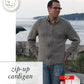 Near a body of water and rocky shore, a man wearing glasses stands outside in a grey Knitbot Zip-Up Cardigan by Never Not Knitting. The image text mentions that it's available in child sizes and describes it as an aran weight cardigan featuring saddle shoulders.