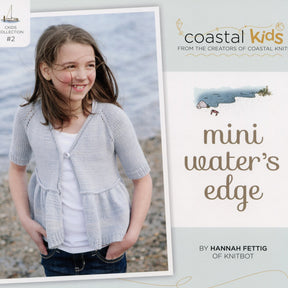 A young girl stands on a rocky shore wearing a light gray cardigan, smiling and looking to the side. The book cover text reads "Coastal Kids from the creators of Coastal Knits," "Mini Water's Edge Cardigan," and "By Hannah Fettig of Knitbot." This is Kids Collection #2 from Never Not Knitting, perfect for any girl's wardrobe.