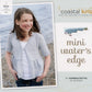 A young girl stands by the seaside wearing a light gray Mini Water's Edge Cardigan over a white shirt. The image graces the cover of a knitting book titled "Coastal Kids Mini Water's Edge Cardigan," authored by Hannah Fettig and available for download. Published under the Never Not Knitting brand, this cardigan is perfect for all seasons and makes an ideal addition to any little girl's wardrobe, with water and rocks providing a picturesque background.