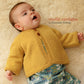 A baby lies on a soft, cream-colored surface, wearing a mustard yellow knitted classic top down cardigan and patterned pants. The text "Mabel's Closet Cradle Cardigan by Never Not Knitting" is written to the right of the baby's head in orange and purple fonts.