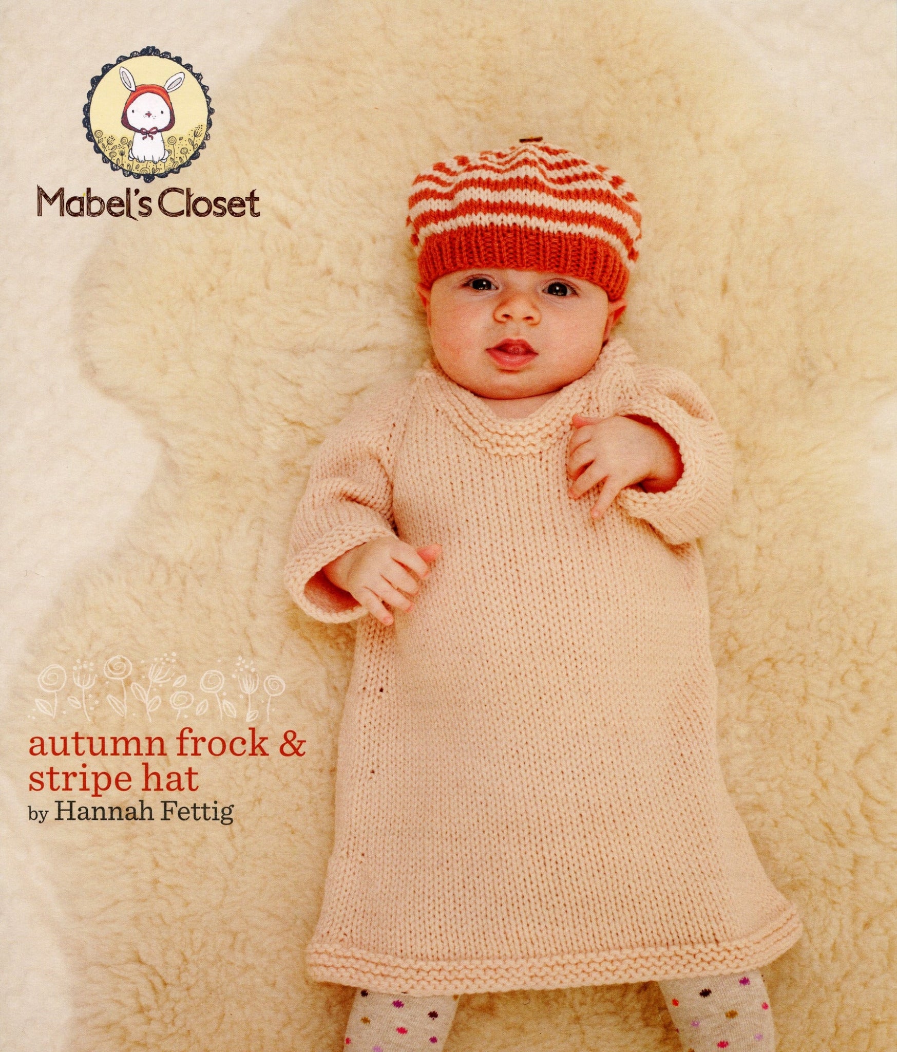 A baby lying on a soft beige surface, wearing a knitted peach dress and a matching stripe hat. The text reads "Never Not Knitting" with a small rabbit logo, and "Mabel's Closet Autumn Frock & Stripe Hat by Hannah Fettig." This warm dress is perfect for your little one.