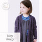 A young girl, the sophisticated little one, is wearing the stylish Knitbot Bitty Breezy Cardigan in dark purple from Never Not Knitting over a gray dress adorned with a colorful bird pattern on the neckline and pocket. She is looking to the side and smiling. The image includes the text "bitty breezy" and describes the cardigan.