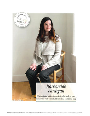 A woman wearing a cozy, light-colored cardigan from Never Not Knitting sits on a wooden chair. The waterfall front style showcases its elegance. Above her head, a logo reads "Knitbot," while below, text states: "Knitbot Harborside Cardigan: This eclectic set-in sleeve design is perfect for the advanced beginner, using worsted weight yarn.