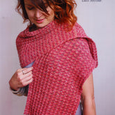 A person with wavy brown and auburn hair stands against a plain background, wearing a textured, pink-toned knitted shawl made from Ella Rae Lace Merino yarn. The ribbed wrap drapes elegantly over the shoulders. Text on the image reads, "Knitting Fever / Euro Yarns" and "Ribbed Wrap - Ella Rae Lace Merino.