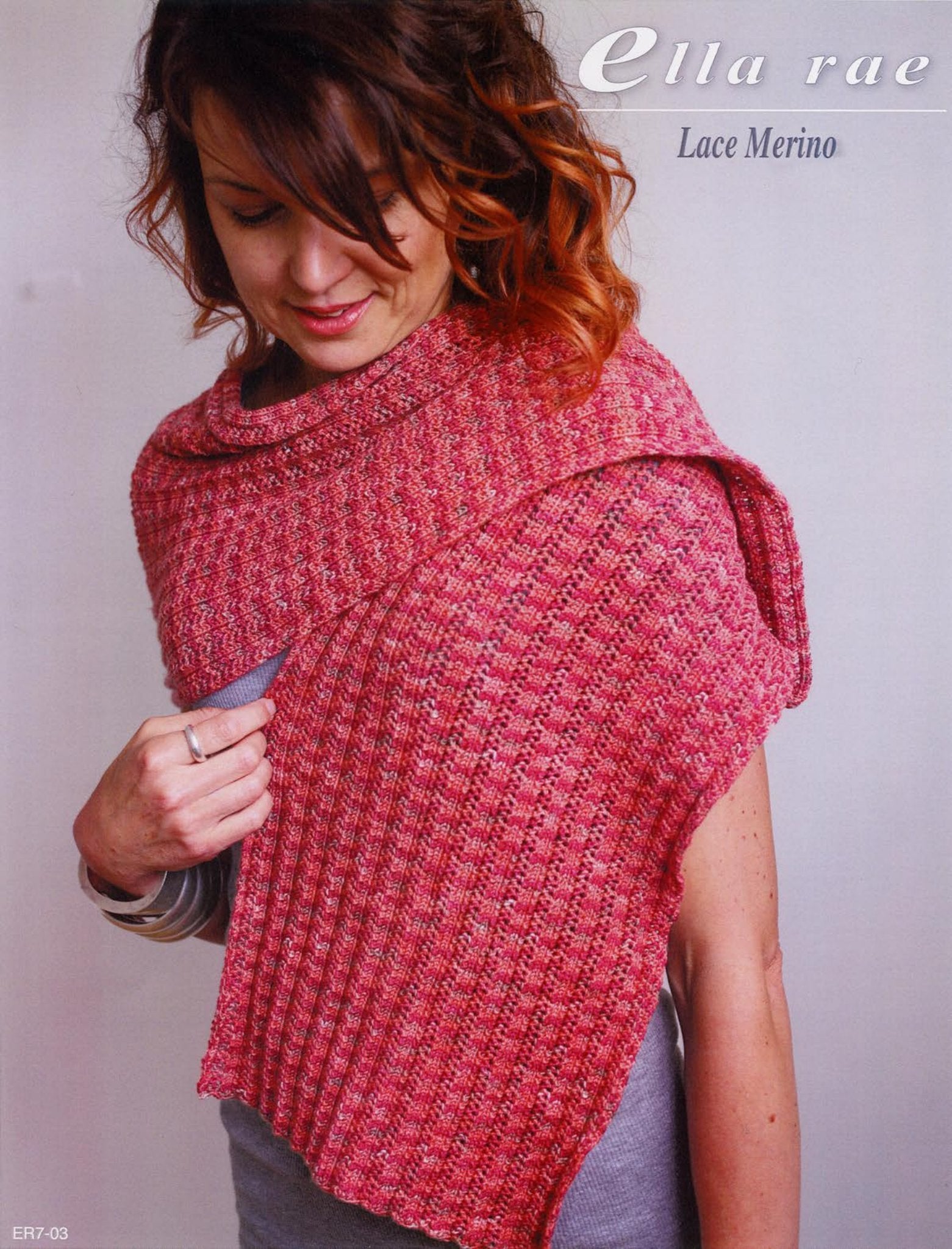 A person with wavy brown and auburn hair stands against a plain background, wearing a textured, pink-toned knitted shawl made from Ella Rae Lace Merino yarn. The ribbed wrap drapes elegantly over the shoulders. Text on the image reads, "Knitting Fever / Euro Yarns" and "Ribbed Wrap - Ella Rae Lace Merino.