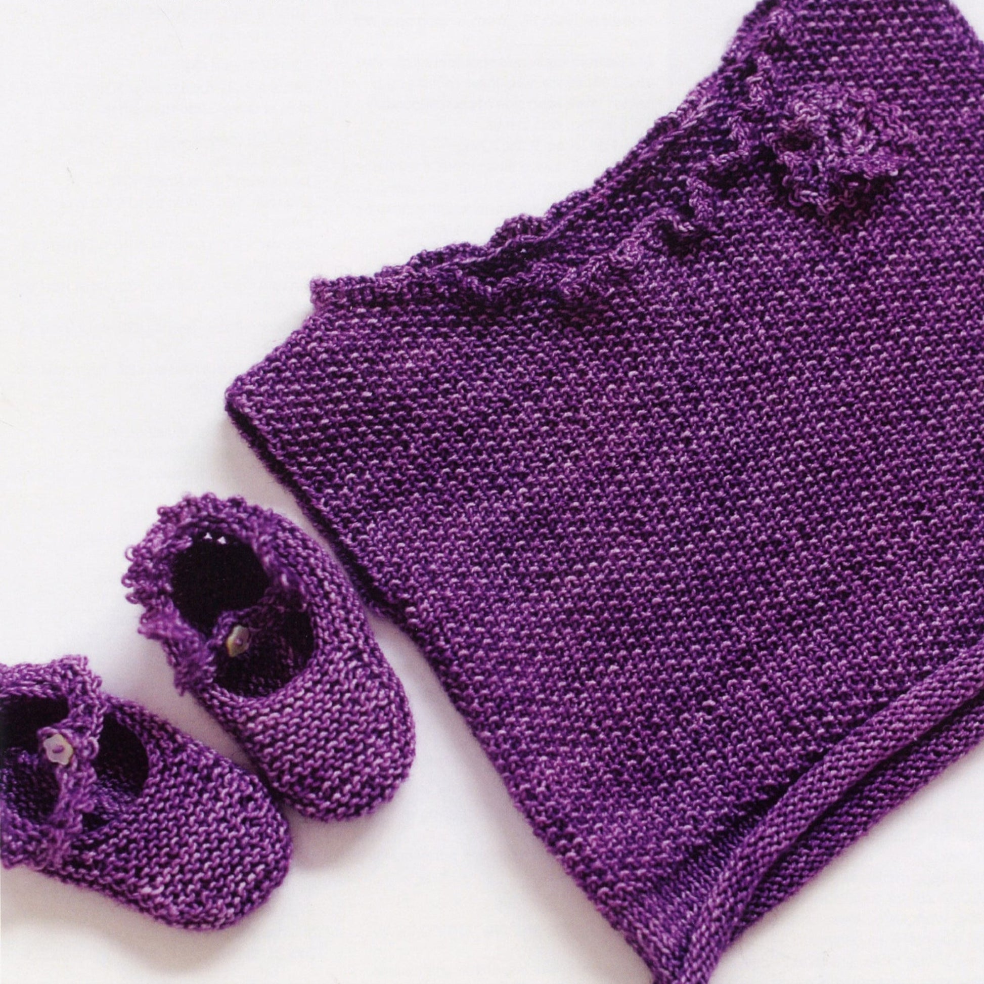 The Baby Booties and Vest - Ella Rae Lace Merino set by Knitting Fever / Euro Yarns includes a charming hand-knitted purple vest with a ruffled collar and matching baby booties, both adorned with decorative flowers, all presented on a white background.