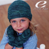 A toddler wearing a knitted teal beanie and mitts set from the Child's Beanie and Mitts - Ella Rae Lace Merino Pattern by Knitting Fever / Euro Yarns smiles at the camera. She is dressed in a light blue shirt with a wooden floor in the background, while the text "Ella Rae Lace Merino" appears in the top right corner.