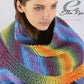 A person is modeling the vibrant, multicolored Ella Rae Seasons Amigo Shawl, crafted from Euro Yarns by Knitting Fever. The shawl features garter stitch stripes in shades of blue, purple, green, yellow, and orange. They appear serene, gazing slightly downward. The text "Ella Rae Seasons" is at the top right corner of the image.