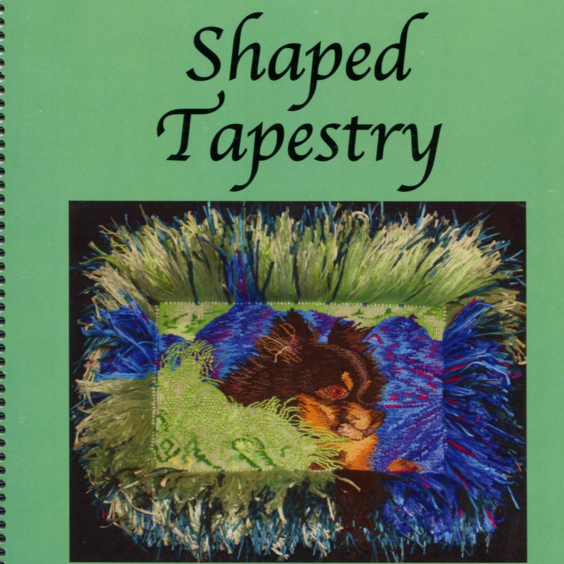 A spiral-bound book titled "Shaped Tapestry 2nd Edition" by Fine Fiber Press, featuring a green background. The cover showcases a non-rectangular tapestry design of a black dog set against a vibrant backdrop of green, blue, and white fringes.