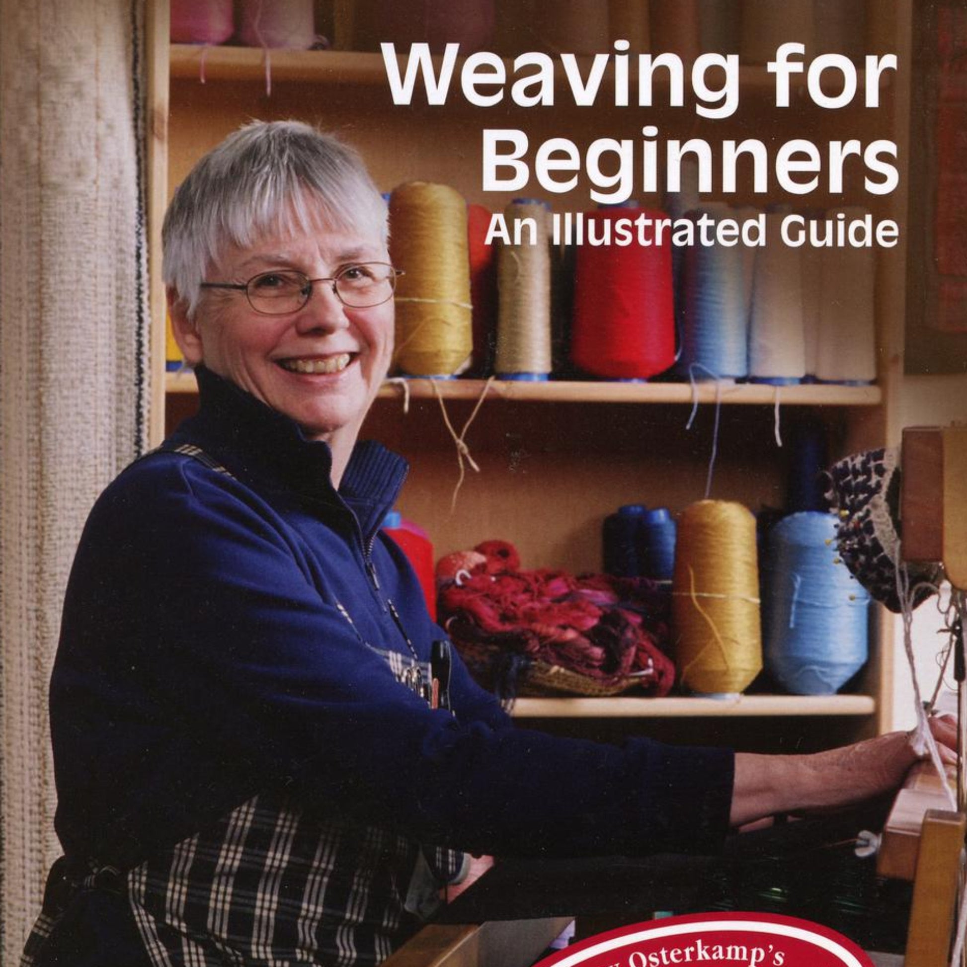 A smiling older woman with short gray hair and glasses is seated at a weaving loom. She is surrounded by colorful yarn spools on shelves behind her. The text at the top reads, "Weaving for Beginners - 2nd Edition" by Lease Sticks Press.