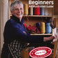 Cover of "Weaving for Beginners - 2nd Edition" by Lease Sticks Press. It features a smiling older woman with short gray hair and glasses, holding a weaving tool while standing by a loom. Brightly colored spools of thread are in the background, ideal for rigid heddle weaving.