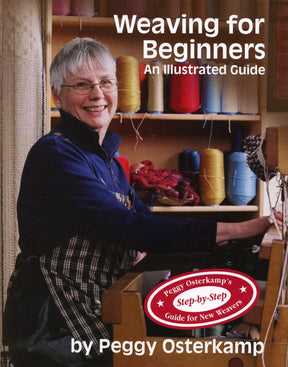 Cover of "Weaving for Beginners - 2nd Edition" by Lease Sticks Press. It features a smiling older woman with short gray hair and glasses, holding a weaving tool while standing by a loom. Brightly colored spools of thread are in the background, ideal for rigid heddle weaving.