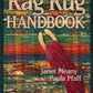 Cover of the "Rag Rug Handbook - 2nd Edition" by Janet Meany and Paula Pfaff, published by Great Northern Weaving. The background showcases a vibrant, woven rug adorned with traditional patterns, while a red fabric and wooden insert tool is prominently placed in the foreground. The title, "Rag Rug Handbook - 2nd Edition," is displayed in large, beige block letters at the top.