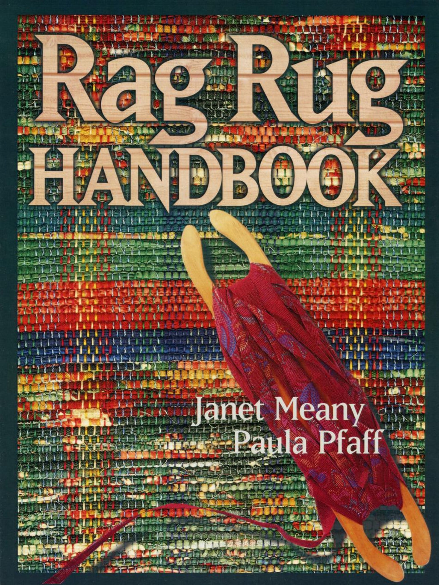 Cover of the "Rag Rug Handbook - 2nd Edition" by Janet Meany and Paula Pfaff, published by Great Northern Weaving. The background showcases a vibrant, woven rug adorned with traditional patterns, while a red fabric and wooden insert tool is prominently placed in the foreground. The title, "Rag Rug Handbook - 2nd Edition," is displayed in large, beige block letters at the top.