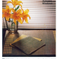 A vibrant vase of orange lilies sits on a wooden table beside folded Handwoven Design Collection #11 heirloom table linens, with sunlight filtering through the closed blinds to cast soft shadows. In the upper right corner, you see "Autumn Windows" in text. The linens are part of Long Thread Media's exquisite collection.