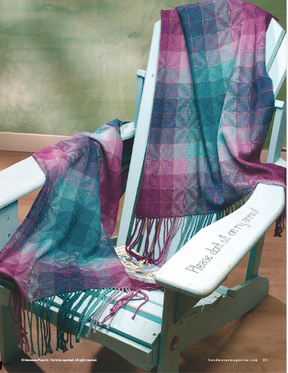 A wooden chair adorned with two vibrant shawls in hues of blue, purple, and pink from the Handwoven Design Collection #19 by Long Thread Media suggests intricate weaving projects. A personalized message and a magazine are partly visible on the seat, set against a soft light green wall that reflects the elegance of Halcyon Yarn craftsmanship.