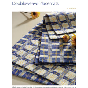 A stack of blue and yellow checkered doubleweave placemats is displayed on a light-colored surface. Several small yellow flowers are scattered around and atop the placemats, adding a touch of decoration. The text reads "Handwoven Special Pattern Collection – 5 Gifts To Weave: eBook Printed Copy by Long Thread Media.