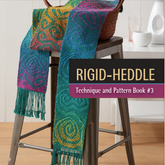 A vibrant woven scarf featuring detailed spiral designs is draped over a wooden chair next to a wall. The book cover reads "Best of Handwoven, Rigid Heddle Technique & Pattern Book 3" by Long Thread Media. In the background, a white vase and a round sculpture can be seen.