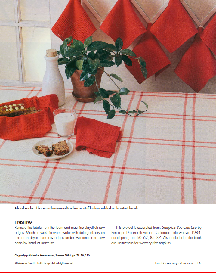 A table set with a red and white checkered tablecloth, red napkins, and a wicker basket of bread creates a cozy vibe. A small potted plant decorates the scene, while the *Best of Handwoven, Reader's Choice: Top Ten Projects from 30 Years of Handwoven* by Long Thread Media offers instructions on using patterns from fabric projects and exploring diverse weaving techniques.