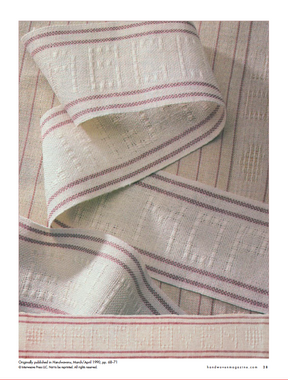 A close-up of a textile from "Best of Handwoven, Reader's Choice: Top Ten Projects from 30 Years of Handwoven eBook (Printed version)" by Long Thread Media reveals a fabric with a soft cream-colored background adorned with thin, parallel burgundy stripes. The intricately woven material is gently folded to showcase its detailed texture and pattern—an excellent choice for household textiles.