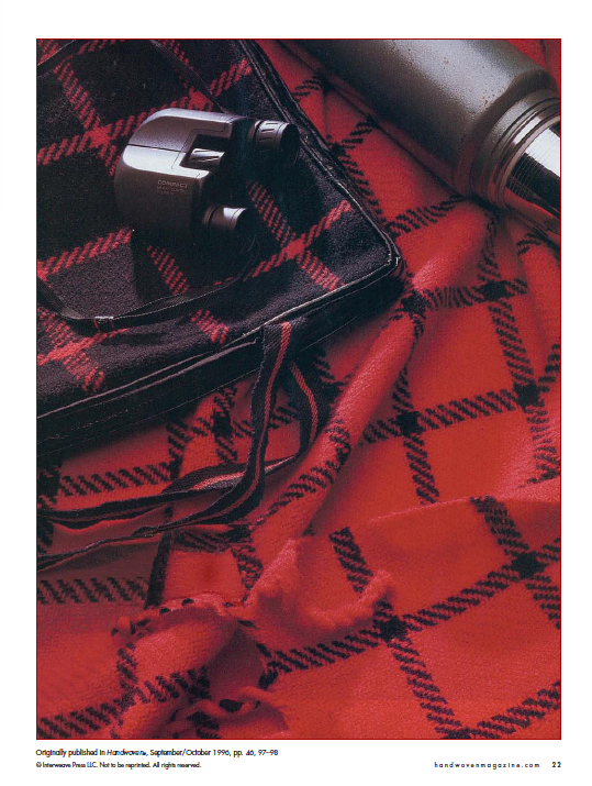 The "Best of Handwoven, Doubleweave, Doublewidth!" eBook by Long Thread Media evokes intricate loom designs with a red and black plaid pattern. Its neatly folded edges offer a casual yet inviting arrangement, perfect for cozy outdoor escapes when accompanied by a pair of binoculars and a metal thermos resting on top.