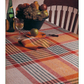 The dining table features a vibrant plaid tablecloth from the "Best of Handwoven, Doubleweave, Doublewidth!" collection by Long Thread Media. It holds a green bottle of wine, a glass of white wine, an apple, and a bowl brimming with fruit such as grapes, pears, and bananas. A wooden chair is partially visible beside the table.