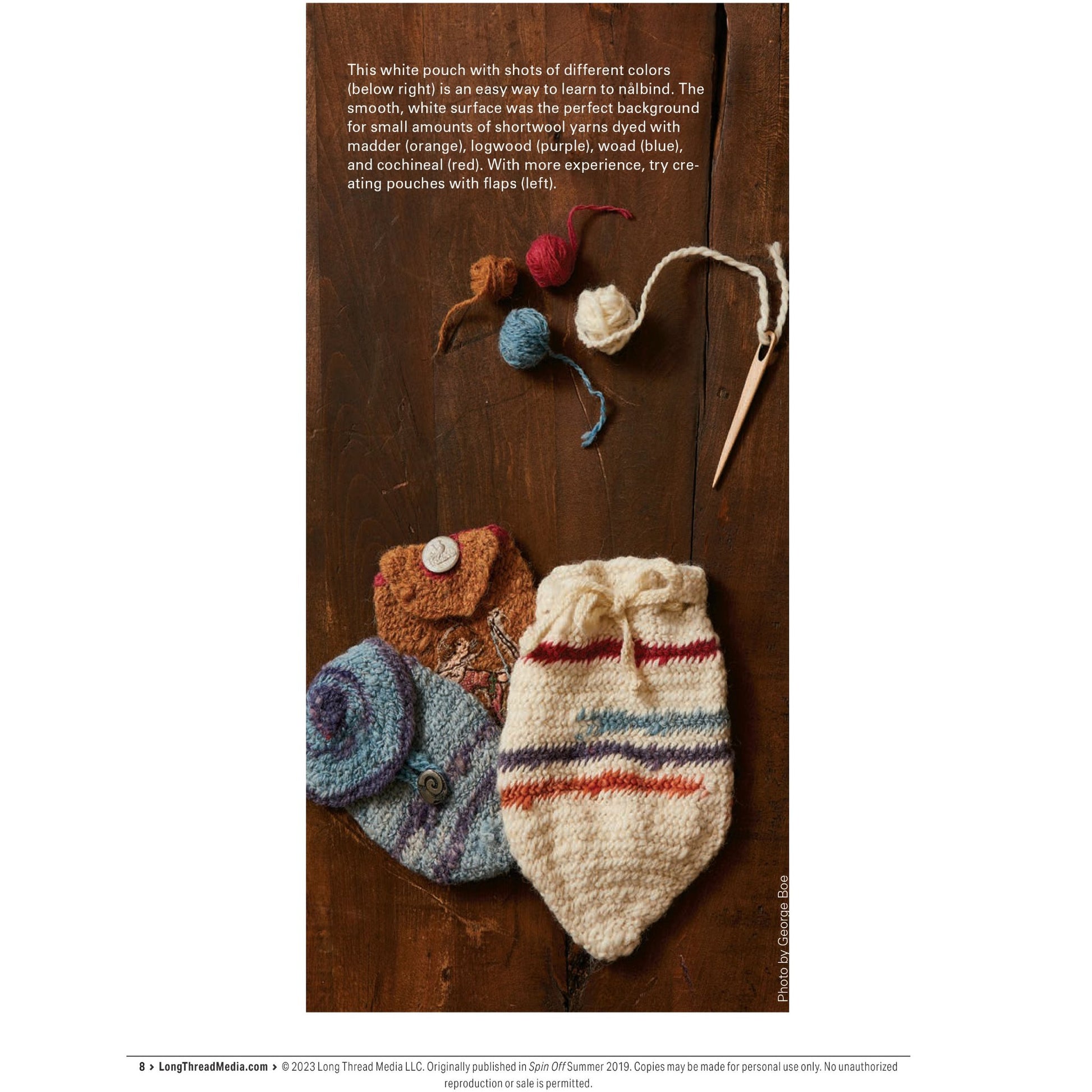 A collection of knit items, displayed on a wooden surface, features several balls of yarn in various colors and thicknesses at the top, a knitting needle, and multiple knitted pouches in different patterns and colors. A white knit pouch with multicolored stripes stands out prominently. This showcase is part of Long Thread Media's PieceWork Presents: Nålbinding Collection: Explore an Ancient Yarn Craft – eBook printed copy.