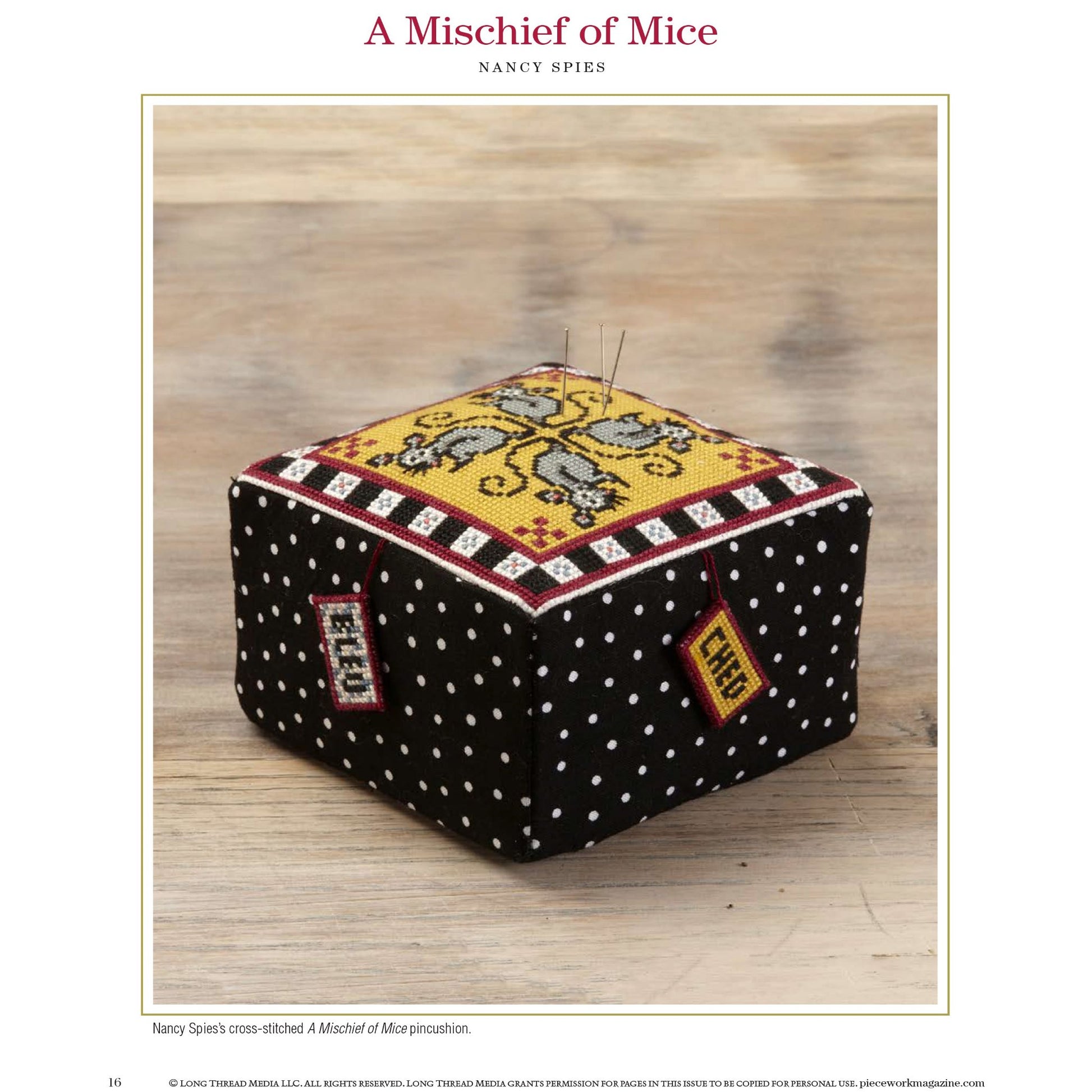 Detailed cross-stitch designs come to life in this cube-shaped pincushion from Long Thread Media's "PieceWork Presents: Pincushions 5 New Pincushion Designs to Bead, Crochet, Tat, Cross-Stitch, and Appliqué: eBook". Featuring Nancy Spies' titled work "A Mischief of Mice," this distinctive pincushion is adorned with a black fabric covered in white polka dots and topped with an intricate cross-stitched image of a mouse.