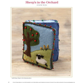 A handmade felt pincushion, designed to resemble an open book, features a green tree adorned with red bead "apples" and a white sheep grazing on grassy hills. The pincushion includes decorative red beading along its edges, with a caption at the top that reads "Sheep's in the Orchard" by Judith Wong. This design is part of the collection presented in the eBook "PieceWork Presents: Pincushions - 5 New Pincushion Designs to Bead, Crochet, Tat, Cross-Stitch, and Appliqué" by Long Thread Media.