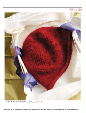 A red knitted cap, created from the "Fall Into Red: 4 Knitting Projects for the Season" eBook by Long Thread Media, rests on white tissue paper surrounded by purple calla lilies, creating an elegant and cozy display.