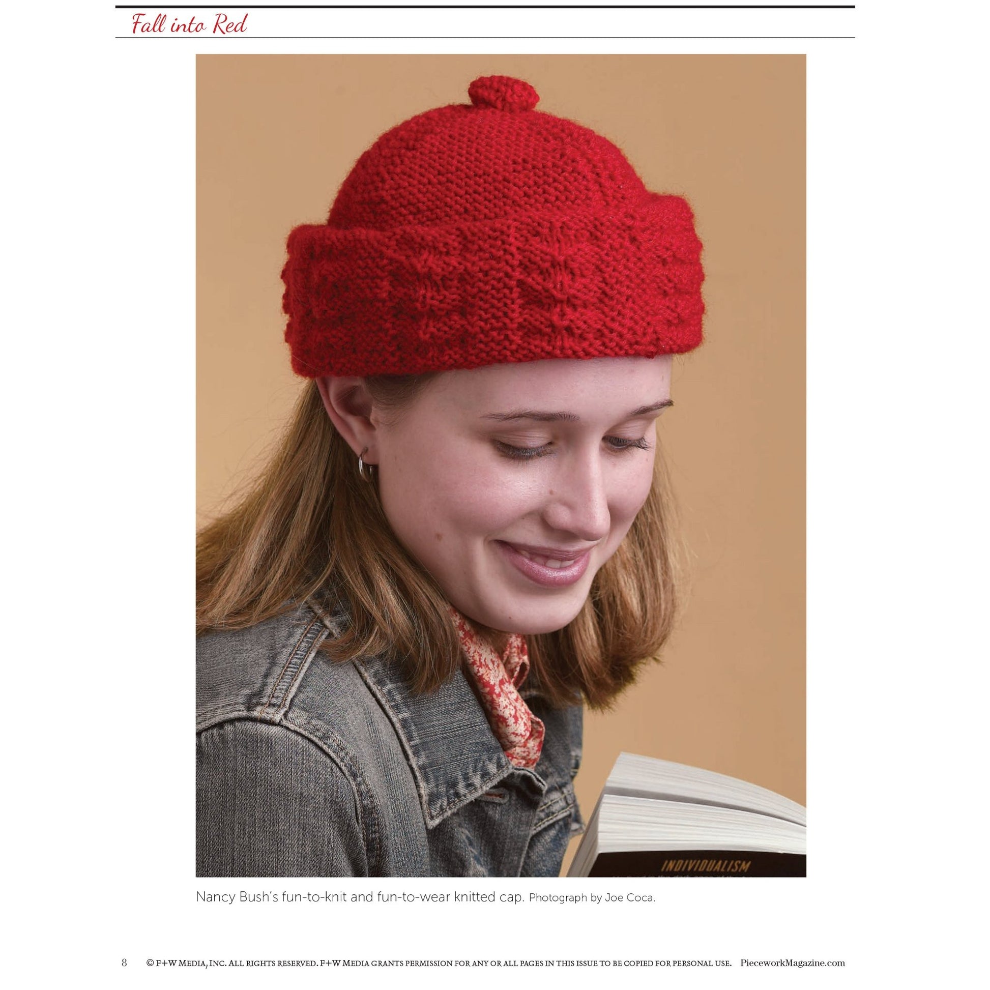 A smiling person is wearing a red knitted hat and a denim jacket. They are looking down at an open book. The background is plain and light brown. Text at the top reads, "Fall Into Red," and a caption at the bottom credits Nancy Bush for the hat design and Joe Coca for the photograph. In addition, check out "Fall Into Red: 4 Knitting Projects for the Season – eBook printed copy" by Long Thread Media for more fantastic fall knitting ideas!