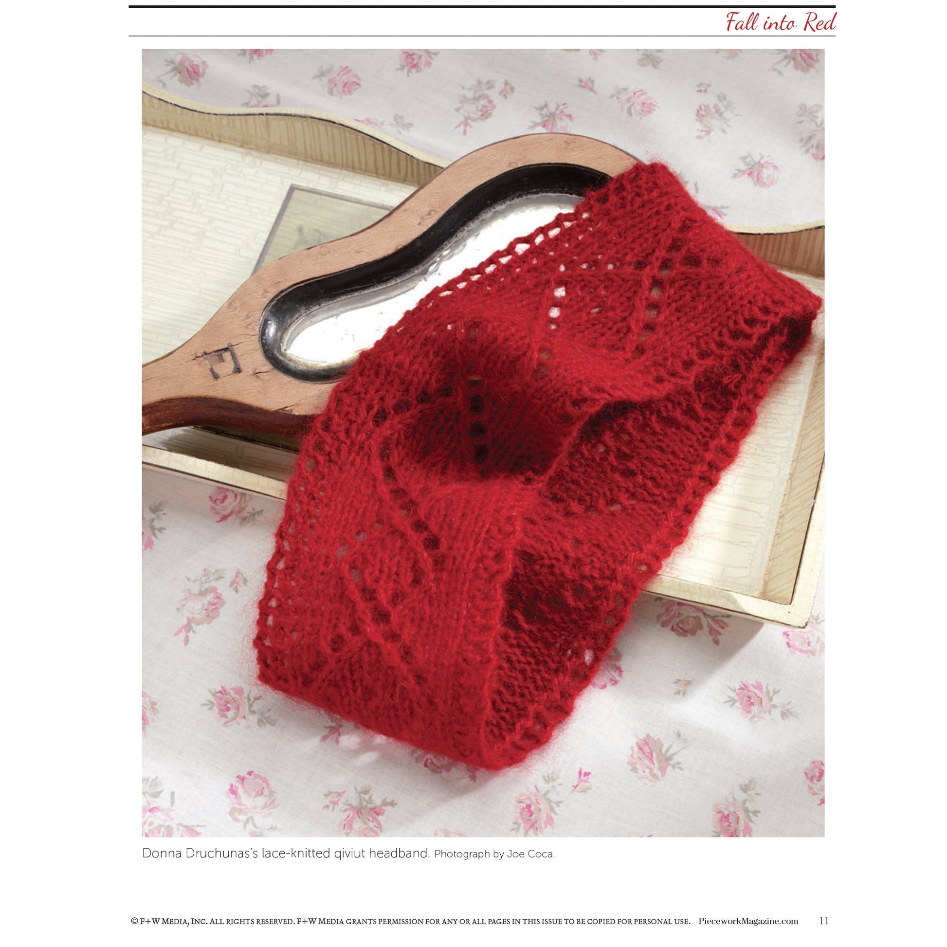 A copy of the printed edition of "Fall Into Red: 4 Knitting Projects for the Season" from Long Thread Media is placed on top of a hand mirror with a wooden handle. The mirror and eBook are set on a fabric background with a delicate floral pattern. The cover displays intricate knitting patterns and adds a pop of vibrant color.