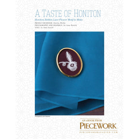 Cover image of "A Taste of Honiton: Honiton Bobbin Lace Flower Motif to Make – eBook printed copy" from Long Thread Media. It features a small, intricate Honiton bobbin lace flower motif set in an oval frame, placed on a bright blue cloth. The text mentions the project designer, Sheila Wills, and photographer, Jo Ann Eaverill.