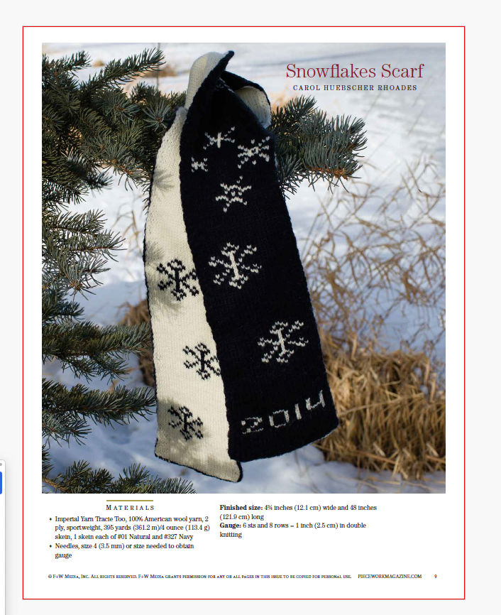 A knitted scarf, included in the "Winter Games: 4 Projects to Knit & More" eBook printed copy by Long Thread Media, is displayed hanging on a pine branch. The design features snowflake patterns with one side black featuring white snowflakes and the year “2014,” while the reverse side is white with black snowflakes, all set against a snowy landscape backdrop.