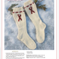 On a snowy surface adorned with pine branches, two knitted cream-colored ski socks featuring red ribbon patterns are showcased. These socks are part of the "Winter Games: 4 Projects to Knit & More – eBook printed copy" by Long Thread Media, with materials and instructions detailed below.