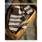 A copy of "Knitting the North: 4 Traditional Mitten Patterns from Northern Europe – eBook printed copy" by Long Thread Media is displayed on an antique wooden suitcase, alongside a pair of brown and cream patterned mittens featuring Nordic-style designs. The text above reads "Orenburg Mittens for Men and Boys.