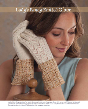 A woman delicately touches her face, adorned with a pair of elegant knitted gloves crafted from the Victorian Lace pattern. These gloves feature intricate lace designs in a two-tone color scheme, with a pristine white top and cuffs in a rich golden brown. Her expression is one of contemplation and serenity.