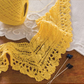 A detailed view showcases a radiant yellow lace border and corner piece intricately knitted, laid out on a wooden surface. Beside it are two knitting needles and a matching ball of yellow yarn. The header text says, "Twin Cable Border and Corner." This piece is inspired by projects from the eBook printed copy "Victorian Lace: 7 Timeless Projects to Knit" by Long Thread Media.