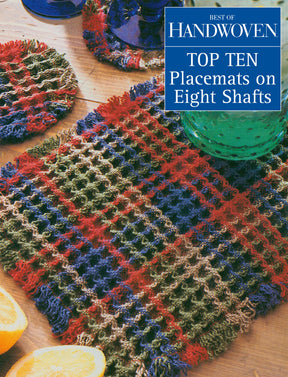 A woven placemat featuring a multicolored plaid pattern in shades of red, blue, and green is showcased on a wooden surface. Several glassware items can be partially seen in the background, while a caption reading "Long Thread Media: Best of Handwoven - Top Ten Placemats on Eight Shafts (Printed Version)" is overlayed.