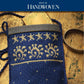 A woven pouch in blue with intricate beige patterns and a celestial design holds a golden card peeking from the top. It rests on a textured wooden surface beside a metal band. The text "Best of Handwoven" is prominently displayed at the top, referencing Long Thread Media's "Best of Handwoven, A Baker's Dozen: 13 Bags to Weave (Printed Version).