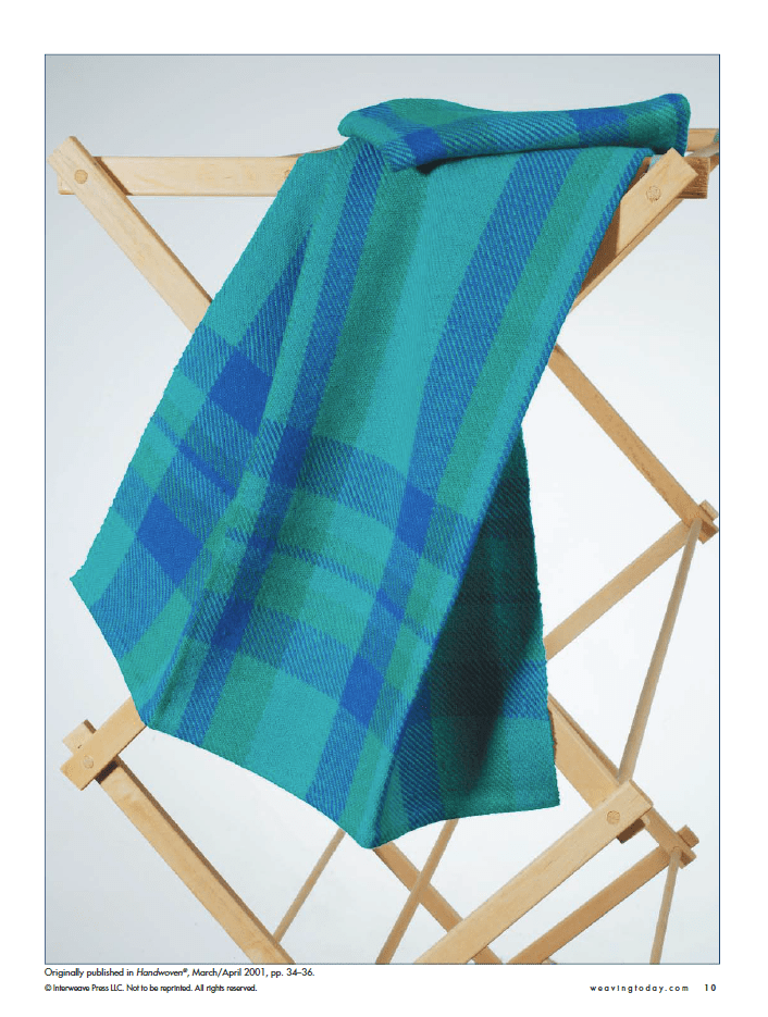 The printed version of Long Thread Media's Best of Handwoven Technique Series: Twills on Four Shafts eBook is elegantly draped over a wooden drying rack, displaying its intricate blue and green plaid patterns.