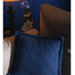 A blue textured pillow with intricate weaving designs sits on a beige couch near a lamp. In the background, a glass dome displays a small traditionally dressed figurine. The scene has a cozy, vintage feel and features Long Thread Media's "Best of Handwoven Technique Series: Twills on Four Shafts" eBook print edition.