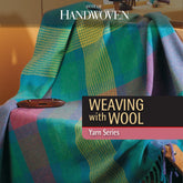 A vibrant plaid woolen blanket is elegantly draped over a chair, highlighting the intricate artistry of wool weaving, with a wooden shuttle placed atop. The text reads "Best of Handwoven Yarn Series: Weaving with Wool: All About Wet Finishing" by Long Thread Media. The setting evokes a warm and cozy textile-themed ambiance.